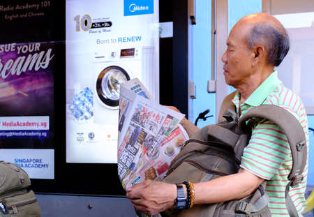Singapore-17 MAR 2018:An old Chinese man reading newspaper at bus stationのeditorial素材
