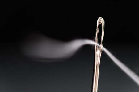 Needle with white thread threaded on black backgroundの写真素材