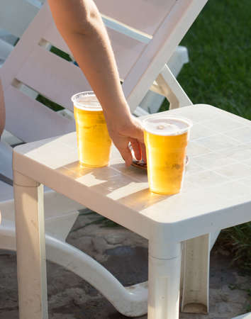 orange beer in transparent plastic glass in man hand closeup outdoorの写真素材