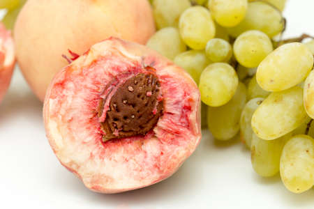 ripe Chinese flat peaches (nectarines) and a bunch of green grapes on white backgroundの写真素材
