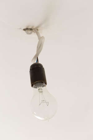 An old light bulb hanging from a white ceilingの写真素材