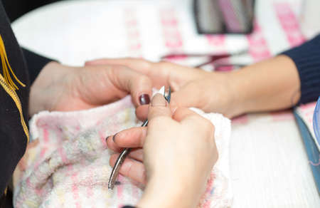 Closeup shot of a woman in a nail salon receiving a manicure by a beautician with nail file. Woman...