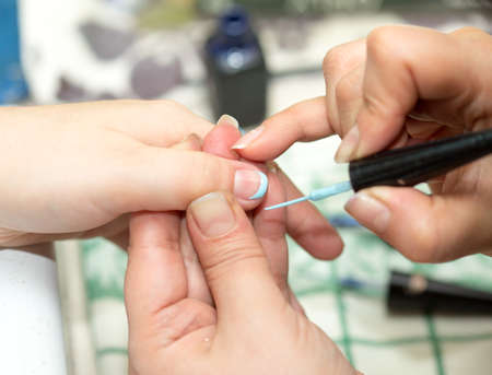 Closeup shot of a woman in a nail salon receiving a manicure by a beautician with nail file. Woman getting nail manicure. Beautician file nails to a customer.の写真素材