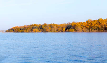 Landscape by the lake with a blue sky, yellow trees on the water with reflectionの写真素材