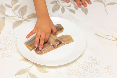 slices of herring on a white plate and baby's handの写真素材