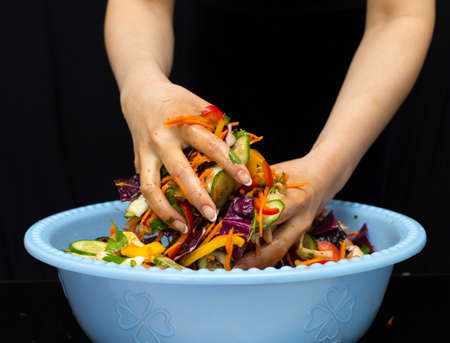 woman preparing salad with fresh vegetables. Preparation of tasty and healthy food on a black backgroundの写真素材