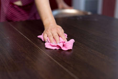 people, homework and housekeeping concept - close up of a woman's hand cleaning table with a tissue...