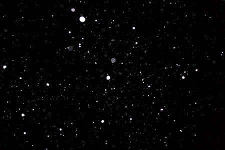 Snowstorm texture. Bokeh lights on black background, shot of flying snowflakes in the airの写真素材