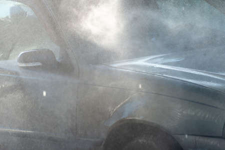 Spraying water from a high pressure hose to the side of a car at a self-service car washの写真素材