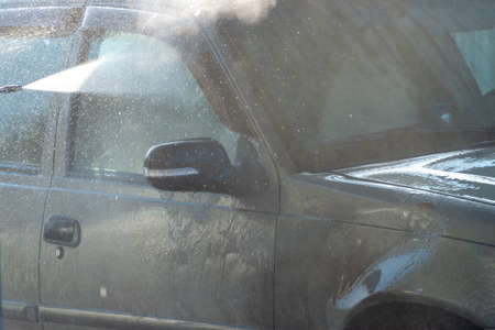 Spraying water from a high pressure hose to the side of a car at a self-service car washの写真素材