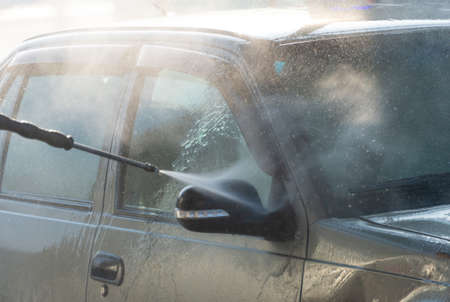 Spraying water from a high pressure hose to the side of a car at a self-service car washの写真素材