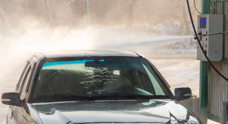 Spraying water from a high pressure hose to the side of a car at a self-service car washの写真素材