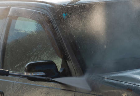 Spraying water from a high pressure hose to the side of a car at a self-service car washの写真素材