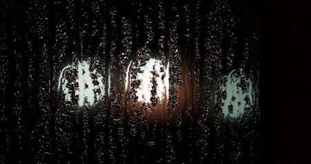 condensate on a transparent glass window and bokeh lights from cars and a red traffic light, on a...