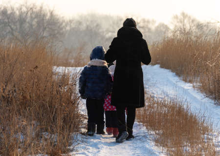 A woman and small children walk in the meadow in winter. They turned away and left.の写真素材
