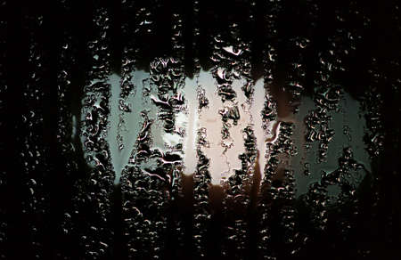 condensate on a transparent glass window and bokeh lights from cars and a red traffic light, on a rainy night view from the car insideの写真素材