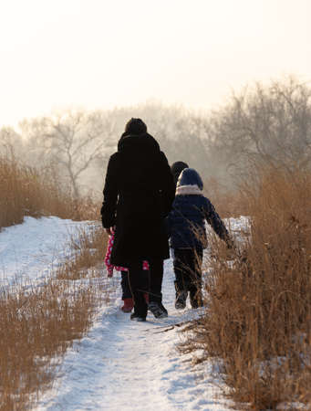 A woman and small children walk in the meadow in winter. They turned away and left.の写真素材