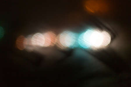 condensate on a transparent glass window and bokeh lights from cars and a red traffic light, on a rainy night view from the car insideの写真素材