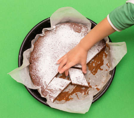 Delicious homemade cake on a green background, top view and the hand of the child wants to take a piece of cakeの写真素材