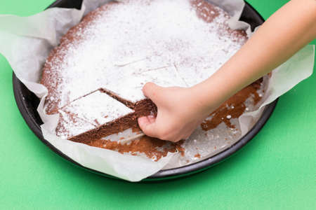 Delicious homemade cake on a green background, top view and the hand of the child wants to take a piece of cakeの写真素材