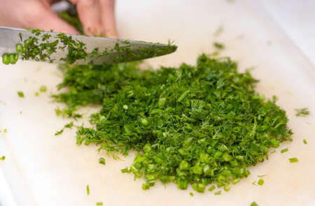 Female hands chopping the dill leaves on a cutting board with a knife. The concept of cookingの写真素材