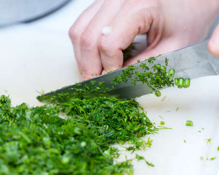 Female hands chopping the dill leaves on a cutting board with a knife. The concept of cookingの写真素材