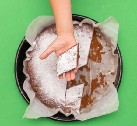 Delicious homemade cake on a green background, top view and the hand of the child wants to take a piece of cakeの写真素材