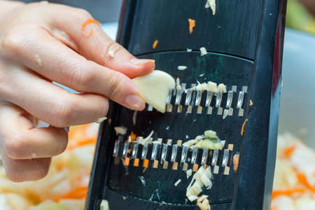 Closeup of cook's hand grated garlic with cabbage salad graterの写真素材