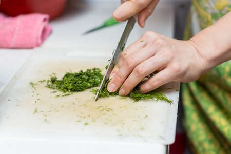 Female hands chopping the dill leaves on a cutting board with a knife. The concept of cookingの写真素材