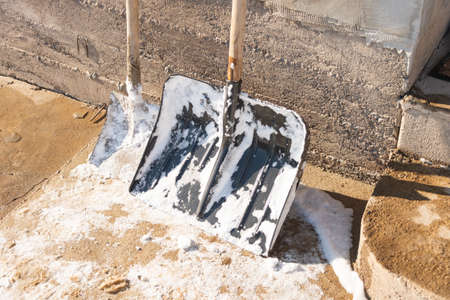 Wide snow shovel against the brick wall on a snowy yard. Severe weather conditions in winterの写真素材