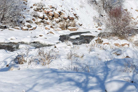 smooth movement of wild water in a river in winter with snow and ice on rocks and stones in beautiful natureの写真素材