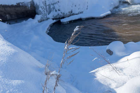 smooth movement of wild water in a river in winter with snow and ice on rocks and stones in beautiful natureの写真素材