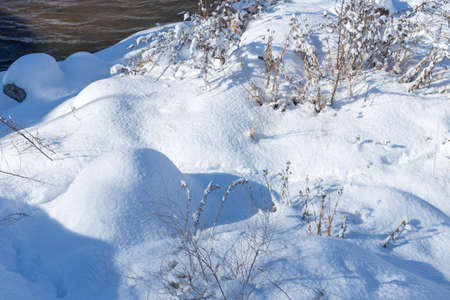 smooth movement of wild water in a river in winter with snow and ice on rocks and stones in beautiful natureの写真素材