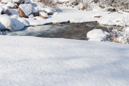 smooth movement of wild water in a river in winter with snow and ice on rocks and stones in beautiful natureの写真素材