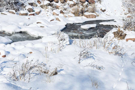 smooth movement of wild water in a river in winter with snow and ice on rocks and stones in beautiful natureの写真素材