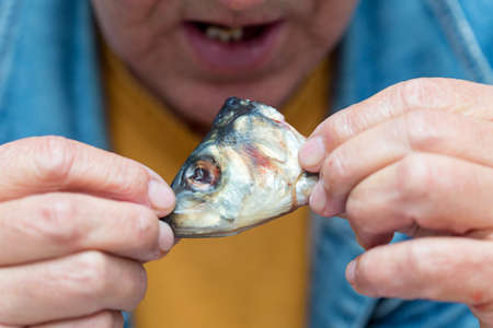 A man holds the head of a fish and is going to eatの写真素材
