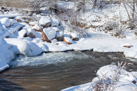 smooth movement of wild water in a river in winter with snow and ice on rocks and stones in beautiful natureの写真素材