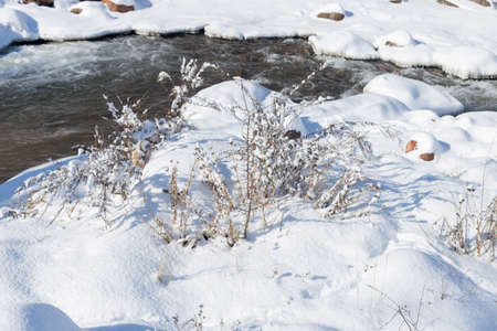 smooth movement of wild water in a river in winter with snow and ice on rocks and stones in beautiful natureの写真素材