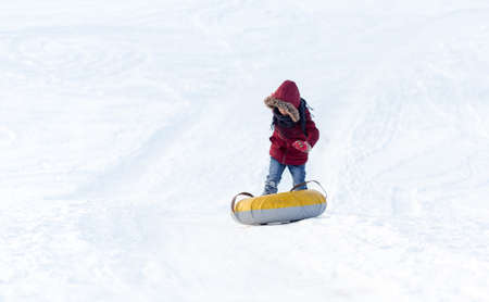 Brave child in red jackets, a trip in the winter from the mountains to tubing. He has an inflatable chamber. It slides quickly through the snow.の写真素材