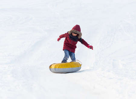 Brave child in red jackets, a trip in the winter from the mountains to tubing. He has an inflatable chamber. It slides quickly through the snow.の写真素材