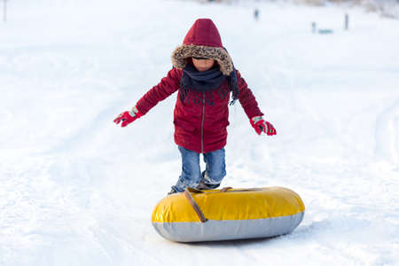 Brave child in red jackets, a trip in the winter from the mountains to tubing. He has an inflatable chamber. It slides quickly through the snow.の写真素材