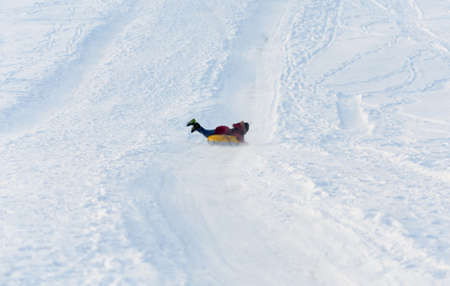 Brave child in red jackets, a trip in the winter from the mountains to tubing. He has an inflatable chamber. It slides quickly through the snow.の写真素材