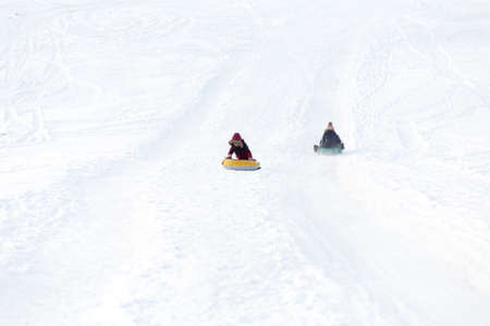 Brave child in red jackets, a trip in the winter from the mountains to tubing. He has an inflatable chamber. It slides quickly through the snow.の写真素材