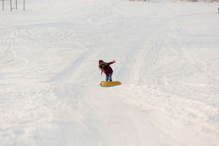 Brave child in red jackets, a trip in the winter from the mountains to tubing. He has an inflatable chamber. It slides quickly through the snow.の写真素材