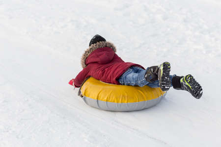 Brave child in red jackets, a trip in the winter from the mountains to tubing. He has an inflatable chamber. It slides quickly through the snow.の写真素材