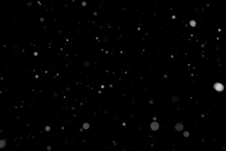 Snowstorm texture. Bokeh lights on black background, shot of flying snowflakes in the airの写真素材