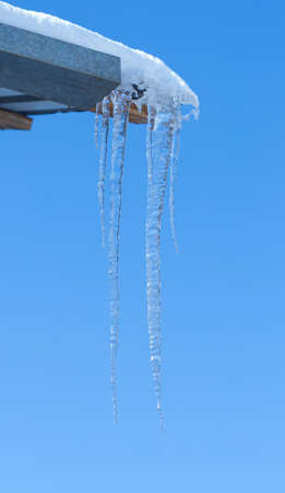 Icicle melts with falling drops on a background of bright blue skyの写真素材