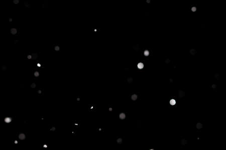 Snowstorm texture. Bokeh lights on black background, shot of flying snowflakes in the airの写真素材