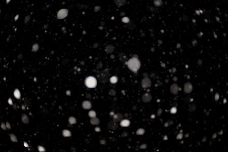 Snowstorm texture. Bokeh lights on black background, shot of flying snowflakes in the airの写真素材