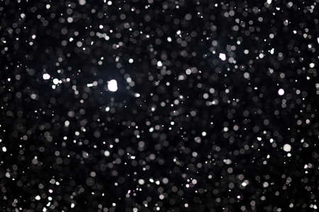 Snowstorm texture. Bokeh lights on black background, shot of flying snowflakes in the airの写真素材
